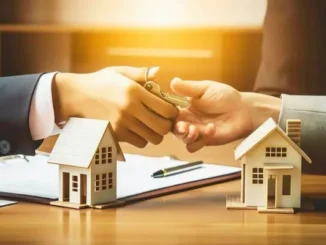 A close-up of a business owner receiving property keys over a desk with miniature house models and loan documents, symbolizing a loan against property.