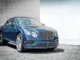 A luxury blue Bentley Continental GT parked on a stone driveway in front of a modern building, representing premium chauffeur services in Amsterdam.