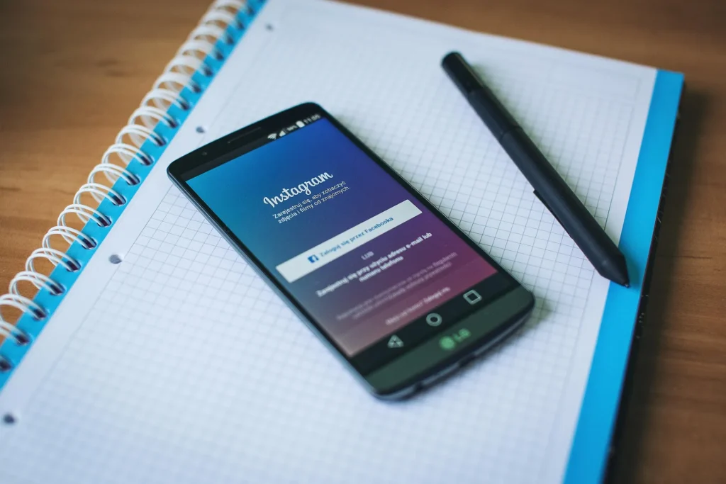 An LG smartphone displaying the Instagram login page in Polish, resting on a spiral-bound grid notebook next to a black pen.