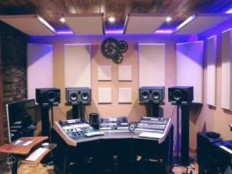 A high-end professional studio workspace featuring strategic acoustic design with wall-mounted sound panels, ceiling baffles, and ergonomic desk setup with purple LED ambient lighting.