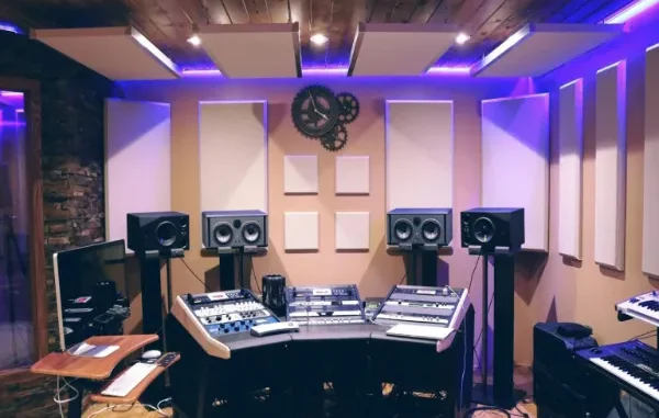 A high-end professional studio workspace featuring strategic acoustic design with wall-mounted sound panels, ceiling baffles, and ergonomic desk setup with purple LED ambient lighting.
