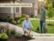 A smiling couple working on their front yard landscaping next to a stone walkway. The woman is kneeling in a flower bed filled with lavender and coneflowers, holding a trowel, while the man stands nearby holding a lawn rake and a bag of premium organic mulch.
