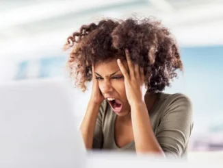 A frustrated female professional holding her head and shouting in front of a laptop, representing the stress of medical billing and lien litigation.