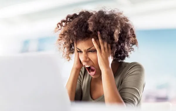 A frustrated female professional holding her head and shouting in front of a laptop, representing the stress of medical billing and lien litigation.