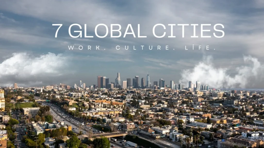 Wide aerial view of a bustling global metropolis skyline with skyscrapers under a partly cloudy sky, featuring overlay text that reads "7 GLOBAL CITIES: WORK. CULTURE. LIFE."