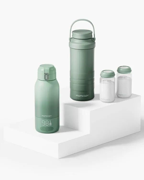 Momcozy sage green portable breast milk warmer with digital temperature display, matching insulated cooler thermos, and two milk storage bottles arranged on a white tiered display.
