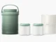 A Momcozy portable breast milk cooler system against a white background, featuring a tall sage green insulated thermos with a handle, two clear glass baby bottles with green lids containing milk, and two stackable white ice packs.