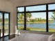 Large black-framed fixed picture windows in a modern bedroom offering an unobstructed scenic view of a lake and palm trees, paired with openable glass patio doors.