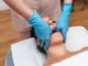A practitioner wearing blue medical gloves performing a physical evaluation or jaw manipulation on a female patient lying down, preparing for TMJ or PRP jaw pain therapy.