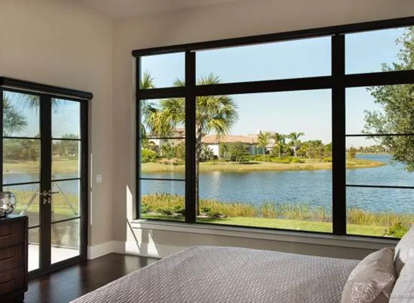 Large black-framed fixed picture windows in a modern bedroom offering a scenic waterfront view, illustrating the style benefits of fixed window designs.