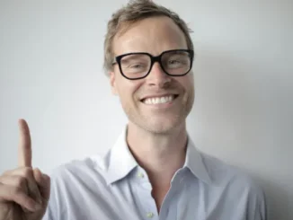 A smiling man with glasses pointing his index finger up, representing a smart betting strategy tip for casino players and punters.