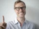 A smiling man with glasses pointing his index finger up, representing a smart betting strategy tip for casino players and punters.