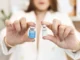 A practitioner holding two small medication vials, Xeomin and Dysport, illustrating the choice between SubQ and IM injection routes for peptide therapy.