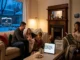 A cozy, well-heated living room in winter where a happy family relaxes together, featuring a smart thermostat set to 71 degrees and a sign outside for Pelican Heating & Air.