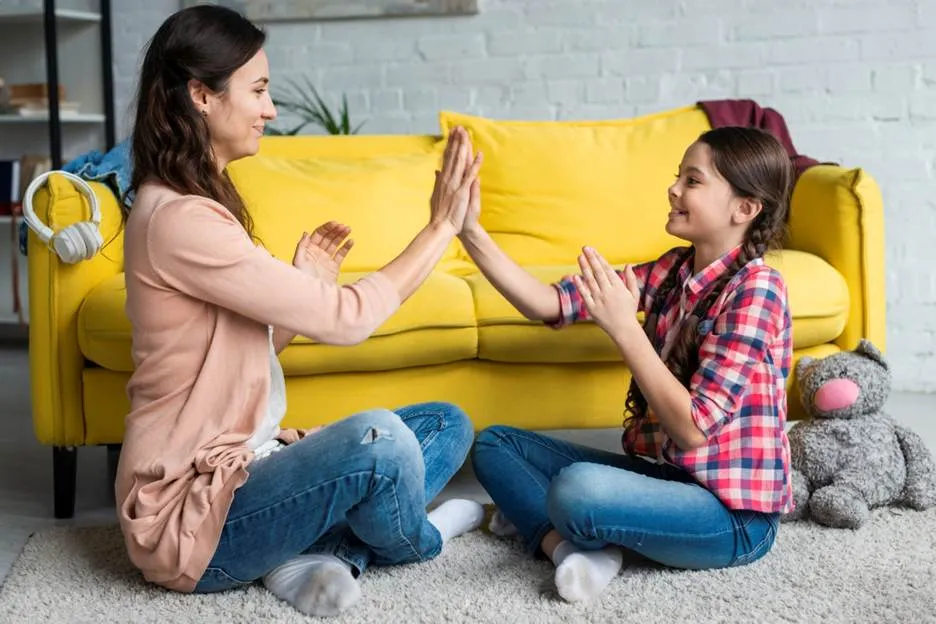An ABA therapist and young girl smiling while giving each other a high-five on the floor in a bright living room.