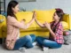 An ABA therapist giving a high five to a young girl sitting cross-legged on the floor in a brightly lit room to reinforce positive behavior.