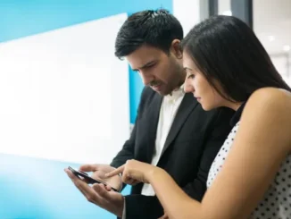 A man and a woman in an office setting looking closely at a smartphone screen, comparing and evaluating features to open a Demat account on a digital trading platform.