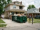 A green ACR Dumpsters roll-off container parked in a suburban driveway filled with construction debris during a residential home renovation.