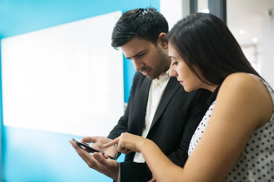 A professional man and woman intently reviewing stock market options on a smartphone to choose the right demat account platform.
