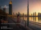 A woman walking along a waterfront promenade in Dubai during a golden sunset, featuring the iconic Burj Khalifa and modern city skyscrapers in the background.