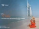 A woman in an orange dress and straw hat sipping a coconut on a sandy Dubai beach with the iconic sail-shaped Burj Al Arab hotel in the background.