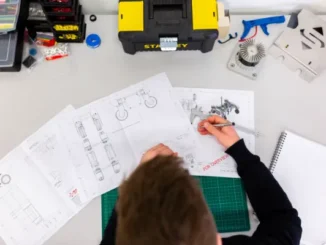 Overhead view of an engineer reviewing technical blueprints and vehicle design schematics at a organized workbench with tools.