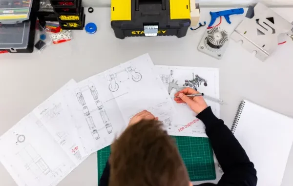 Overhead view of an engineer reviewing technical blueprints and vehicle design schematics at a organized workbench with tools.
