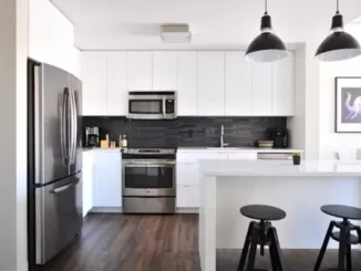 A modern kitchen featuring a stainless steel appliance package including a French door refrigerator, slide-in electric range oven, over-the-range microwave, and built-in dishwasher against white cabinets and a black tile backsplash.