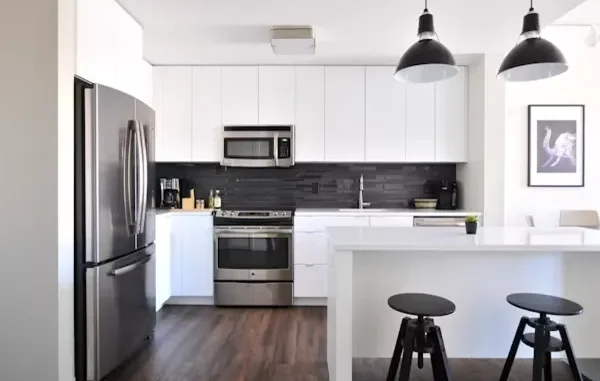 A modern kitchen featuring a stainless steel appliance package including a French door refrigerator, slide-in electric range oven, over-the-range microwave, and built-in dishwasher against white cabinets and a black tile backsplash.