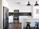 A modern kitchen featuring a stainless steel appliance package including a French door refrigerator, slide-in electric range oven, over-the-range microwave, and built-in dishwasher against white cabinets and a black tile backsplash.