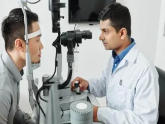 An optometrist in an eye hospital using a slit lamp microscope to examine a patient's eyes for vision problems.