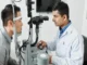 An optometrist in an eye hospital using a slit lamp microscope to examine a patient's eyes for vision problems.