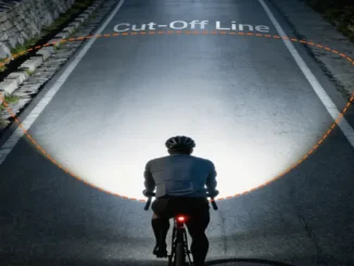 Cyclist riding at night with a front lamp bike light showing a wide road beam pattern and an anti-glare cut-off line.