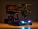 Black Golden folding mobility scooter featuring illuminated LED headlights, armrests, and a front storage basket.