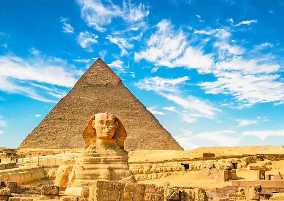 The Great Sphinx standing in front of the massive Pyramid of Khafre under a bright blue sky in Giza, Egypt.