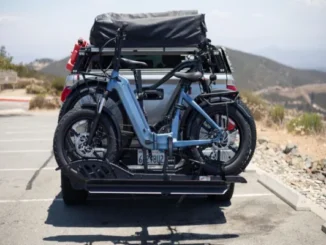 Rear view of a pickup truck with a heavy-duty platform hitch bike rack carrying two blue electric fat-tire bicycles parked at an outdoor viewpoint.