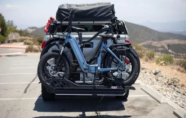 Rear view of a pickup truck with a heavy-duty platform hitch bike rack carrying two blue electric fat-tire bicycles parked at an outdoor viewpoint.