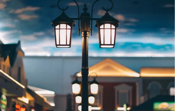 A double-lantern vintage style outdoor street lamp illuminated at twilight against a modern building backdrop.