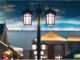 A double-lantern vintage style outdoor street lamp illuminated at twilight against a modern building backdrop.