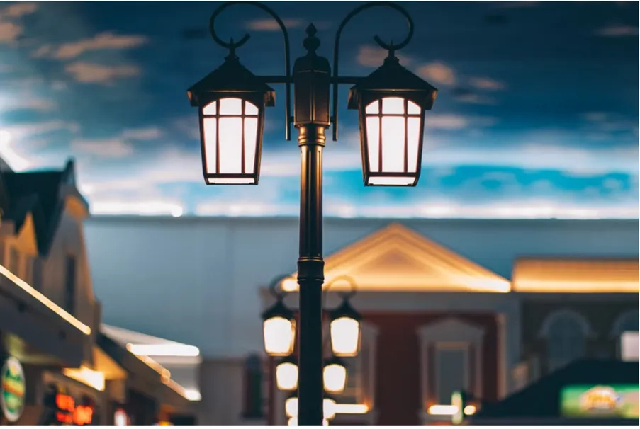 A classic double-lantern street lamp illuminating a paved outdoor walkway at twilight.