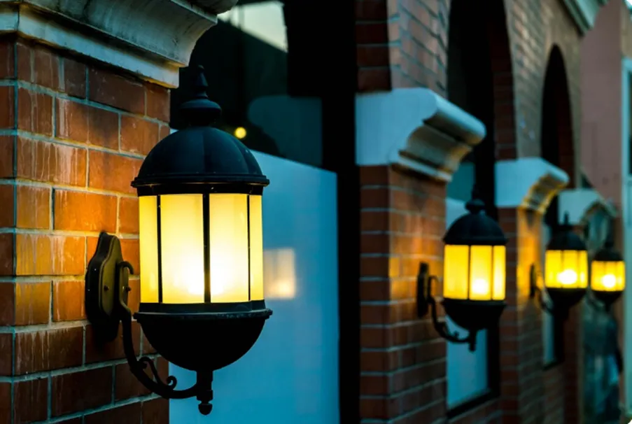 Row of elegant vintage-style outdoor wall lanterns casting a warm glow along a red brick building exterior.