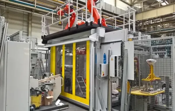 High-speed machine protection door with yellow borders and clear windows safeguarding an automated robotic work cell in an industrial manufacturing plant.