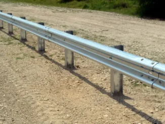 Galvanized steel W-beam highway guardrail installed along a dirt shoulder to prevent vehicle run-off-road accidents.