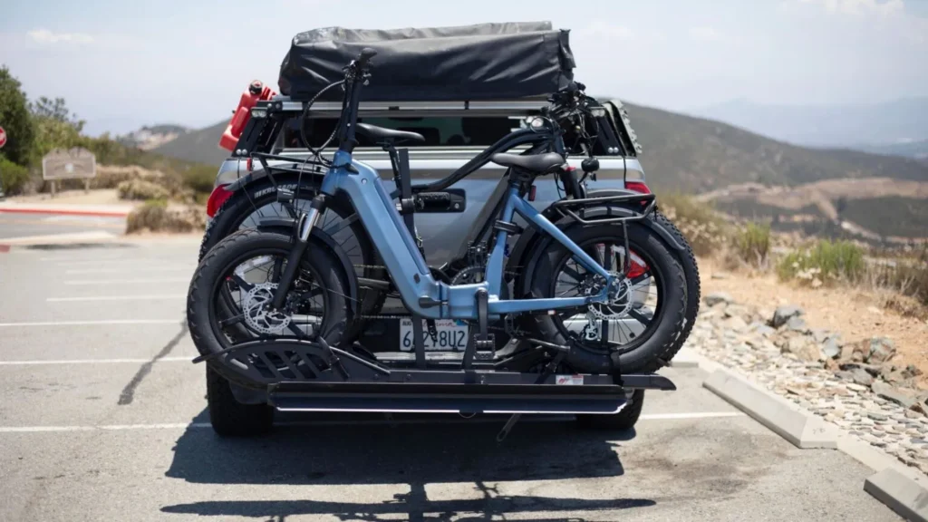 Rear view of a silver pickup truck with a heavy-duty hitch bike rack holding two blue fat-tire electric bikes parked outdoors.