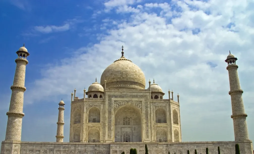 The white marble Taj Mahal mausoleum in Agra under a bright blue sky with scattered clouds, highlighting bespoke travel experiences on a tailor-made India tour.