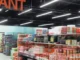 Suspended linear IP65 LED tri-proof light fixtures illuminating retail store aisles and merchandise shelves from an industrial ceiling.