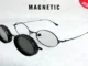Round black-rimmed eyeglasses with a matching magnetic clip-on sunglass attachment hovering to the side to demonstrate how they snap on.