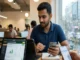 A man in a cafe looking at a tablet displaying a Cricbet99 dashboard showing 2026 bonus deals and cashback offers, while holding a smartphone and pen.