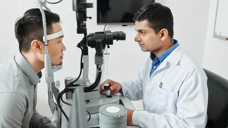 An optometrist examining a patient's eyes using a slit lamp microscope in a clinical setting.