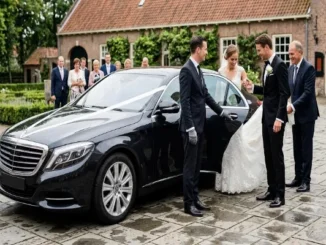 A candid photograph capturing a wedding couple boarding a black Mercedes-Benz S-Class sedan. A formally dressed chauffeur holds the door, with the groom helping the bride. The setting is a paved courtyard of a European venue in the Netherlands, with blurred VIP guests in the background. Natural daylight.
